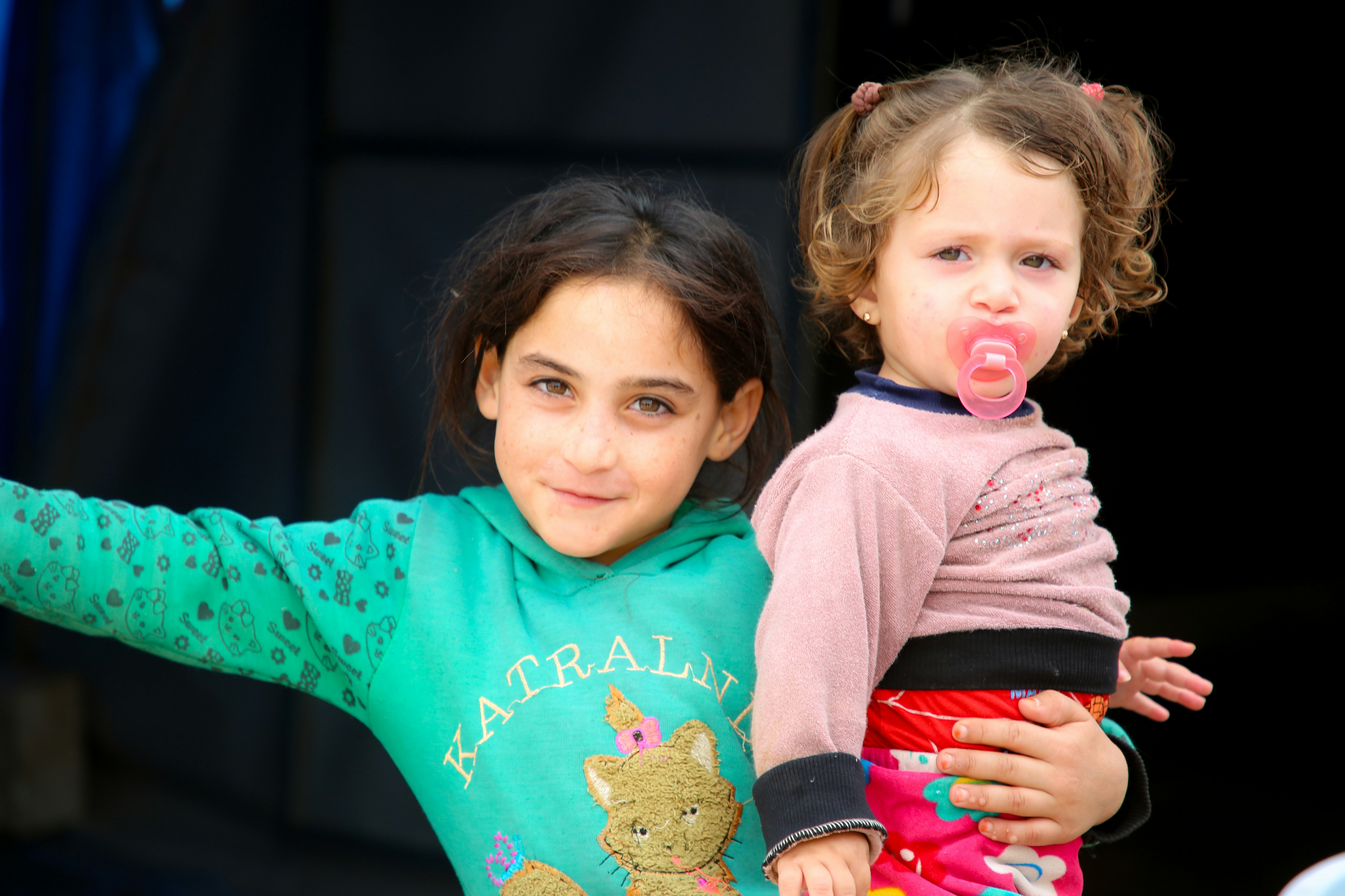 Two sisters hugging and looking at the camera.